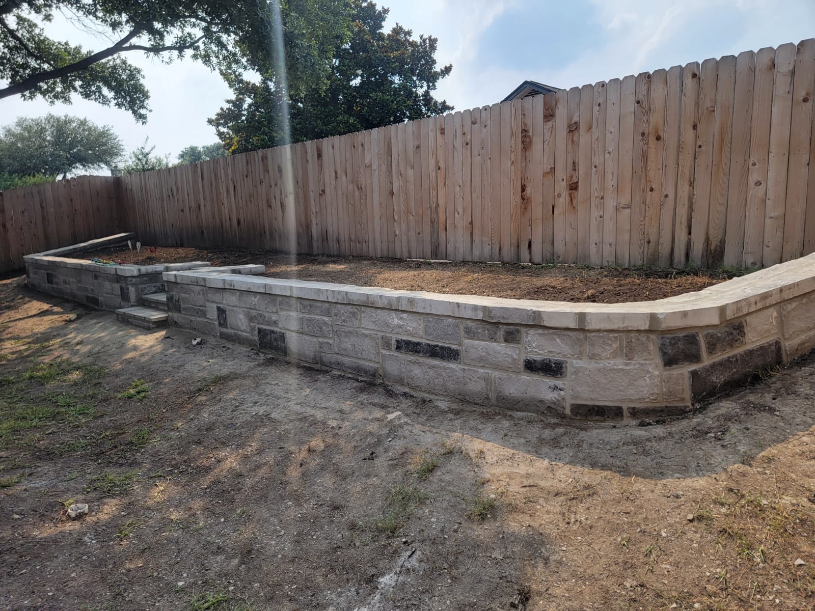 Finished retaining wall with integrated steps and stone cap in a fenced backyard