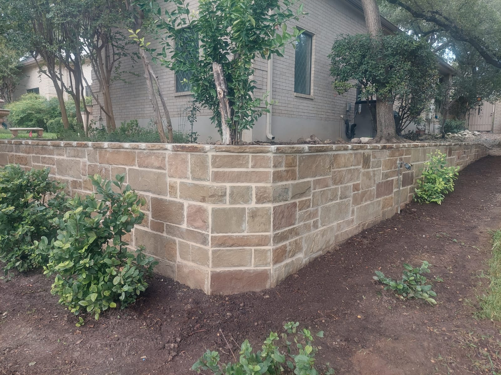 Stone retaining wall wrapping a landscaped yard with shrubs